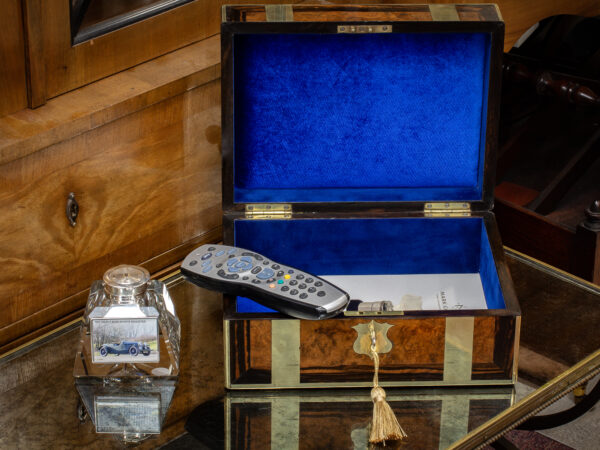 Overview of the Antique Victorian Walnut & Coromandel Jewellery Box in a decorative collectors setting containing a tv remote and magazine